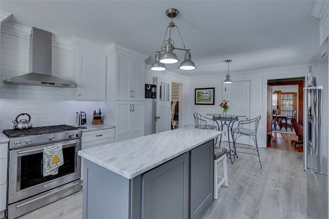 kitchen featuring white cabinetry, light wood-type flooring, backsplash, wall chimney range hood, and appliances with stainless steel finishes