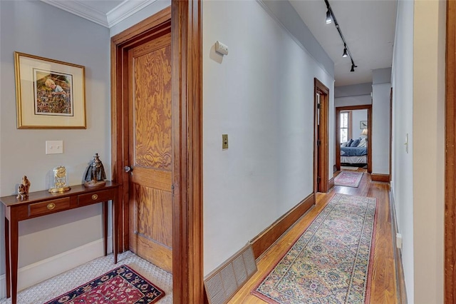hall featuring visible vents, light wood finished floors, rail lighting, baseboards, and ornamental molding