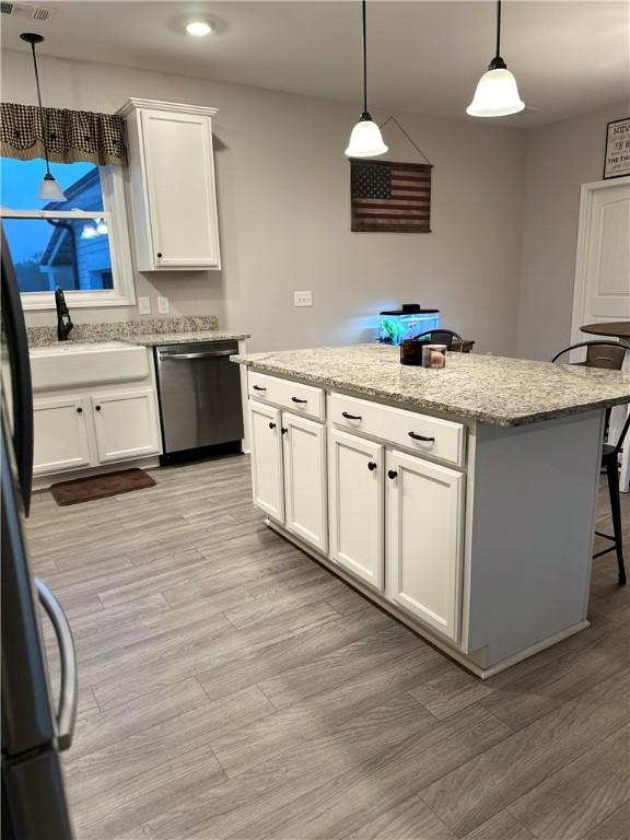 kitchen with stainless steel dishwasher, a center island, a sink, white cabinets, and light stone counters