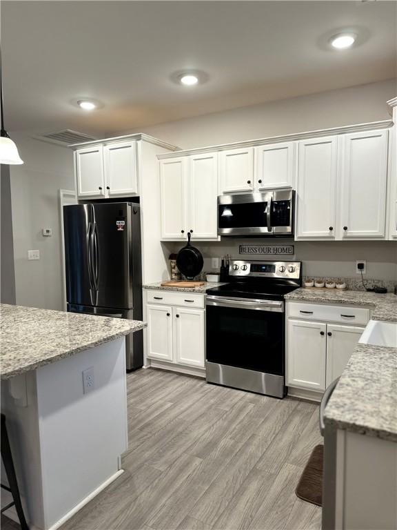 kitchen with stainless steel appliances, white cabinets, light wood-type flooring, light stone counters, and recessed lighting