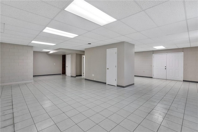 empty room with baseboards, concrete block wall, and a drop ceiling