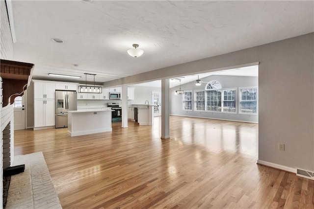 unfurnished living room with visible vents, light wood finished floors, a fireplace, a ceiling fan, and vaulted ceiling
