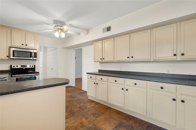 kitchen featuring cream cabinetry, dark countertops, appliances with stainless steel finishes, and visible vents