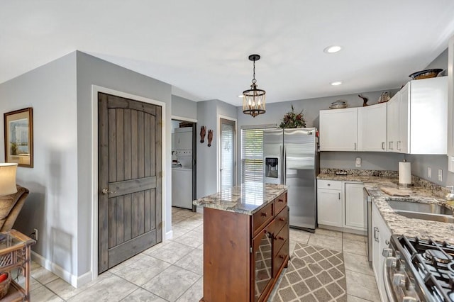 kitchen with white cabinets, stainless steel appliances, a sink, light stone counters, and a center island