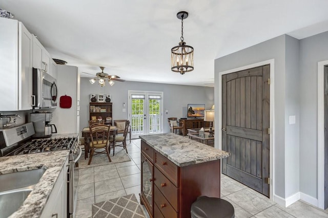 kitchen with white cabinets, stainless steel appliances, a kitchen island, ceiling fan with notable chandelier, and french doors