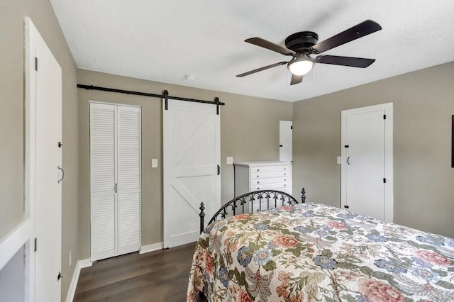 bedroom with a closet, baseboards, ceiling fan, dark wood finished floors, and a barn door