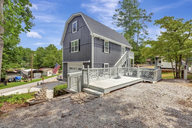 back of house featuring a gambrel roof, a garage, stairway, and a shingled roof