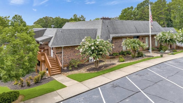 view of front of home featuring brick siding, stairway, uncovered parking, and a shingled roof