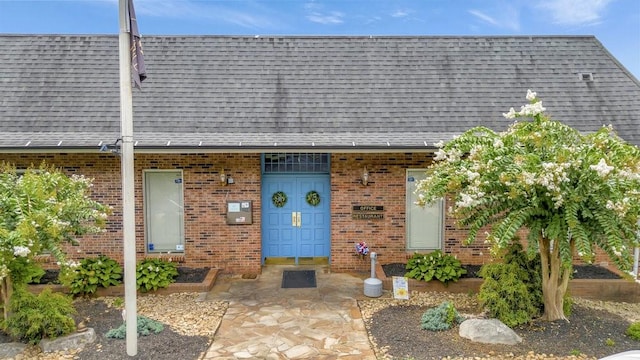 doorway to property featuring brick siding and roof with shingles