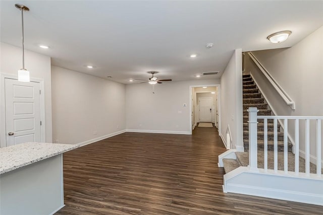 unfurnished living room featuring baseboards, dark wood-style flooring, stairs, and a ceiling fan