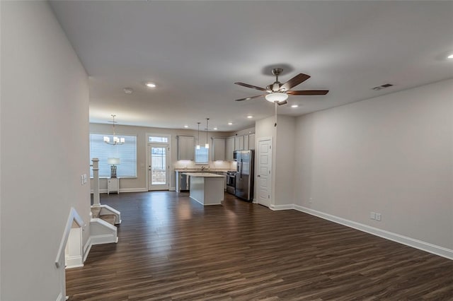 unfurnished living room with dark wood-style flooring, ceiling fan with notable chandelier, baseboards, and recessed lighting