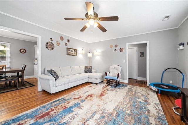 living area featuring crown molding, ceiling fan, visible vents, wood finished floors, and baseboards