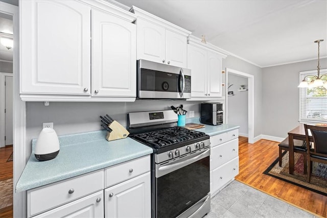 kitchen with white cabinets, light countertops, crown molding, stainless steel appliances, and pendant lighting