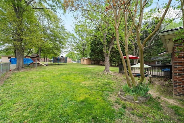 view of yard with a trampoline, fence, a playground, a storage unit, and an outbuilding