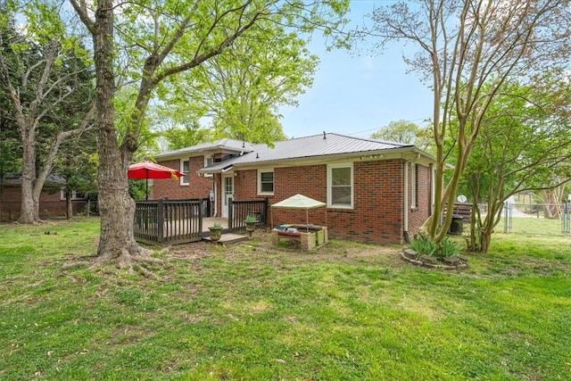 rear view of house featuring a yard, metal roof, fence, brick siding, and a deck