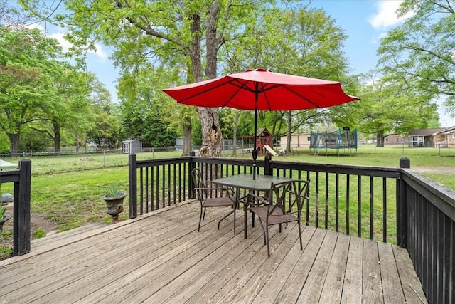 wooden deck featuring a trampoline, a shed, an outbuilding, a playground, and a lawn