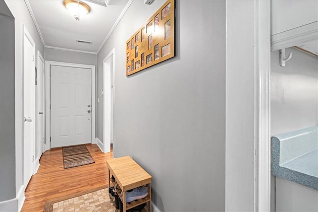 doorway with crown molding, visible vents, baseboards, and light wood-style floors