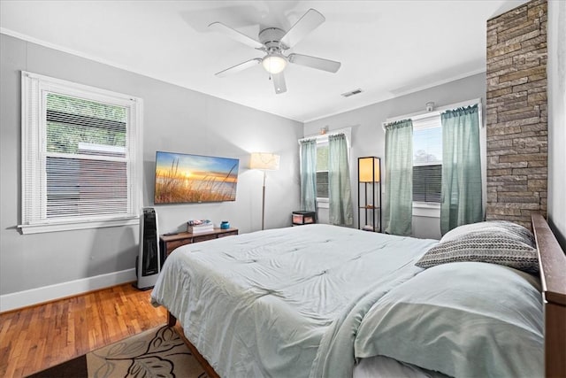 bedroom featuring ceiling fan, light wood-type flooring, ornamental molding, visible vents, and baseboards