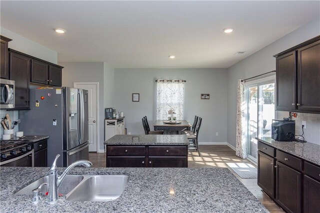 kitchen with a sink, dark brown cabinetry, backsplash, light stone counters, and appliances with stainless steel finishes