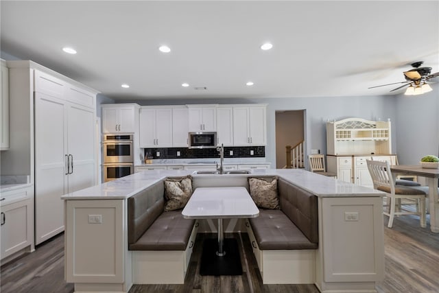 kitchen featuring decorative backsplash, stainless steel appliances, dark wood finished floors, a center island with sink, and a sink