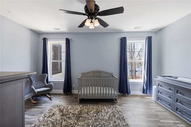 bedroom with visible vents, a crib, and wood finished floors