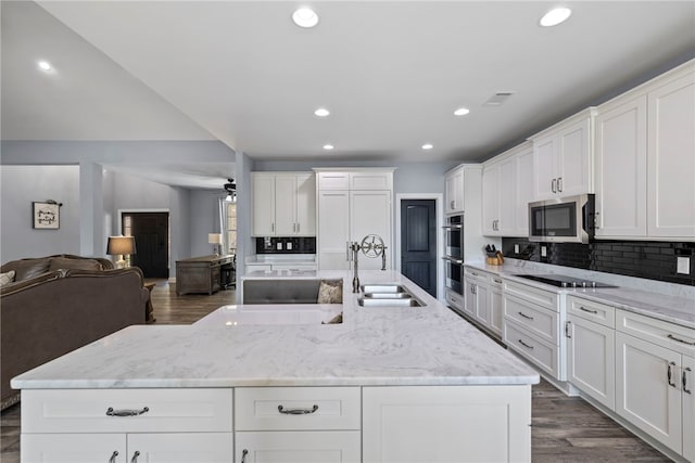 kitchen featuring open floor plan, white cabinetry, stainless steel appliances, a center island with sink, and a sink