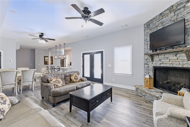 living room with a ceiling fan, wood finished floors, a stone fireplace, baseboards, and visible vents