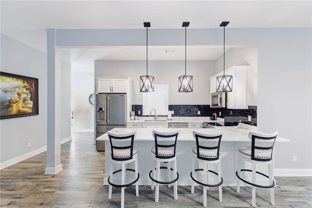 kitchen featuring light countertops, backsplash, a breakfast bar area, appliances with stainless steel finishes, and white cabinets