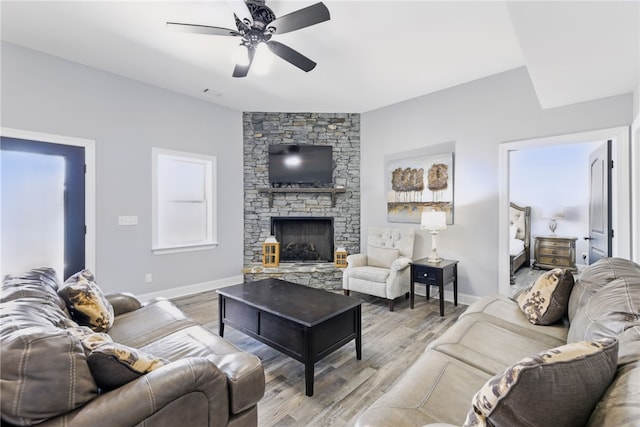 living area featuring light wood-style flooring, baseboards, a fireplace, and ceiling fan