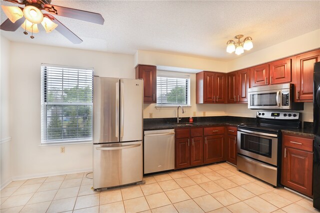 kitchen with a sink, dark countertops, light tile patterned floors, and appliances with stainless steel finishes