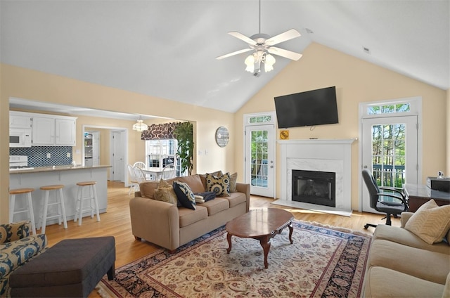 living room featuring light wood-type flooring, ceiling fan, a premium fireplace, and high vaulted ceiling
