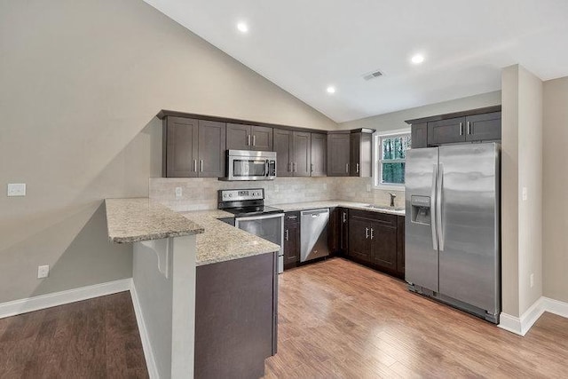 kitchen featuring dark brown cabinetry, light stone counters, a peninsula, and appliances with stainless steel finishes