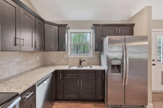 kitchen with stainless steel appliances, tasteful backsplash, dark brown cabinetry, a sink, and vaulted ceiling