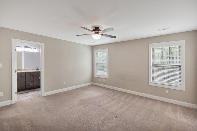 unfurnished bedroom featuring ensuite bath, baseboards, light colored carpet, and visible vents