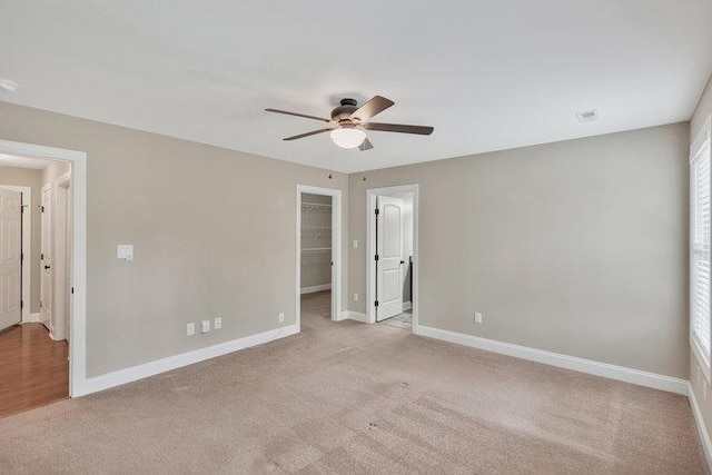 unfurnished bedroom featuring a spacious closet, a closet, baseboards, and light colored carpet