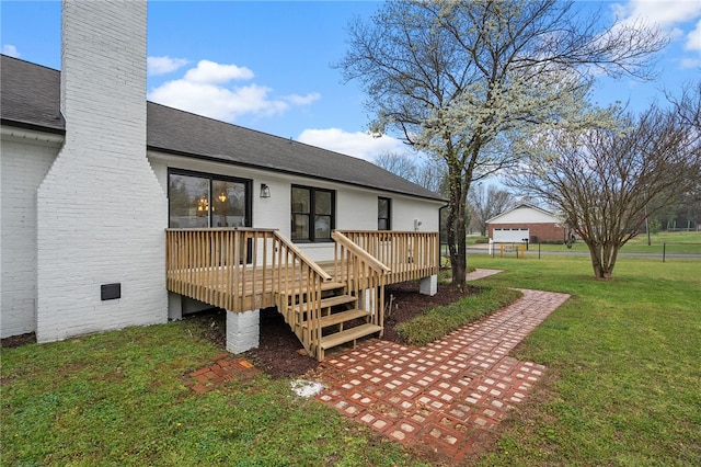 exterior space with a chimney, roof with shingles, a yard, and a wooden deck