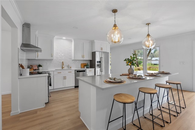 kitchen with white cabinets, a breakfast bar, appliances with stainless steel finishes, a sink, and wall chimney range hood