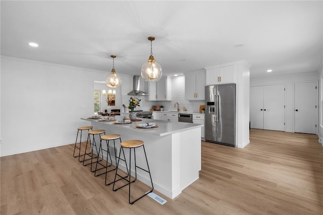 kitchen with backsplash, a kitchen bar, appliances with stainless steel finishes, light wood-type flooring, and wall chimney range hood