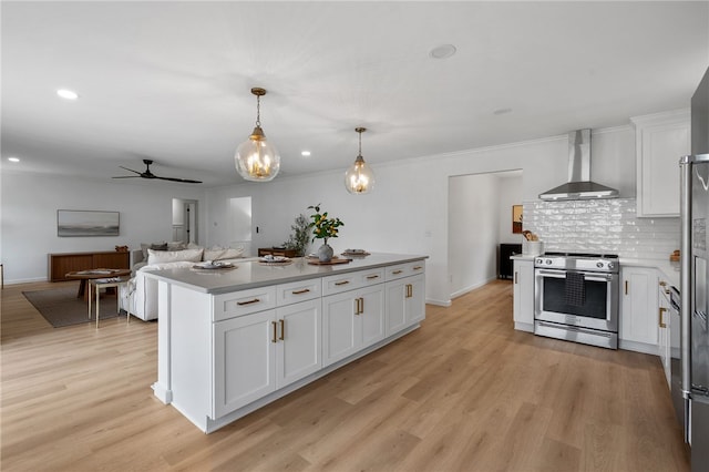 kitchen featuring wall chimney exhaust hood, stainless steel range with electric cooktop, a ceiling fan, white cabinetry, and light wood-type flooring