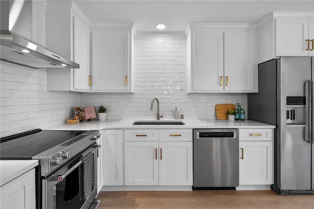 kitchen with white cabinetry, light countertops, a sink, appliances with stainless steel finishes, and wall chimney exhaust hood