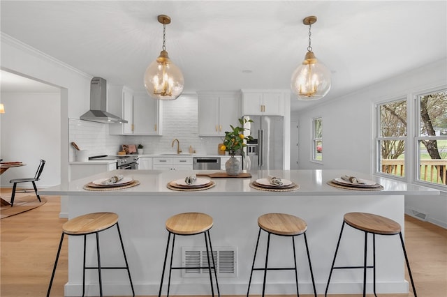 kitchen featuring a breakfast bar, visible vents, wall chimney range hood, and appliances with stainless steel finishes