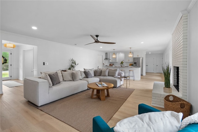 living room with light wood-style flooring, crown molding, a brick fireplace, ceiling fan, and recessed lighting