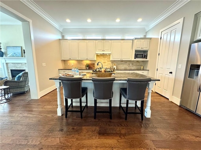 kitchen with under cabinet range hood, crown molding, appliances with stainless steel finishes, and backsplash