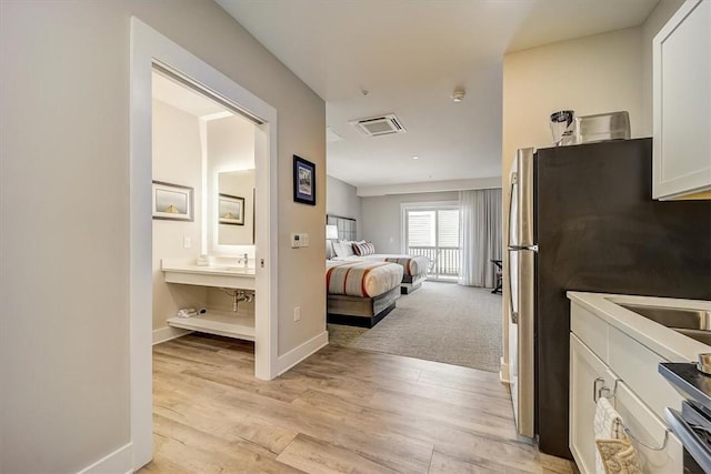 interior space with light wood-style flooring, freestanding refrigerator, ensuite bath, and baseboards
