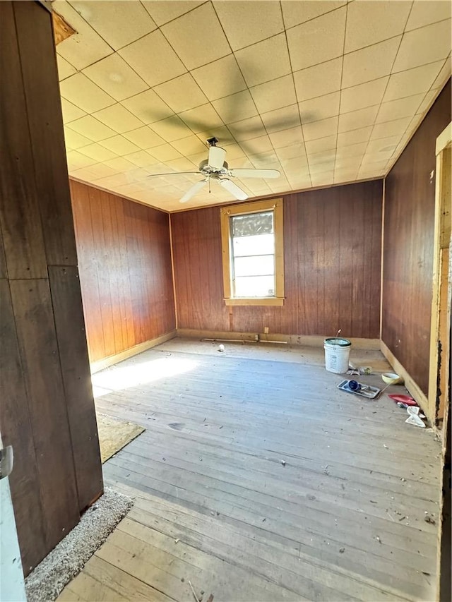 unfurnished room featuring wood-type flooring, wooden walls, and a ceiling fan