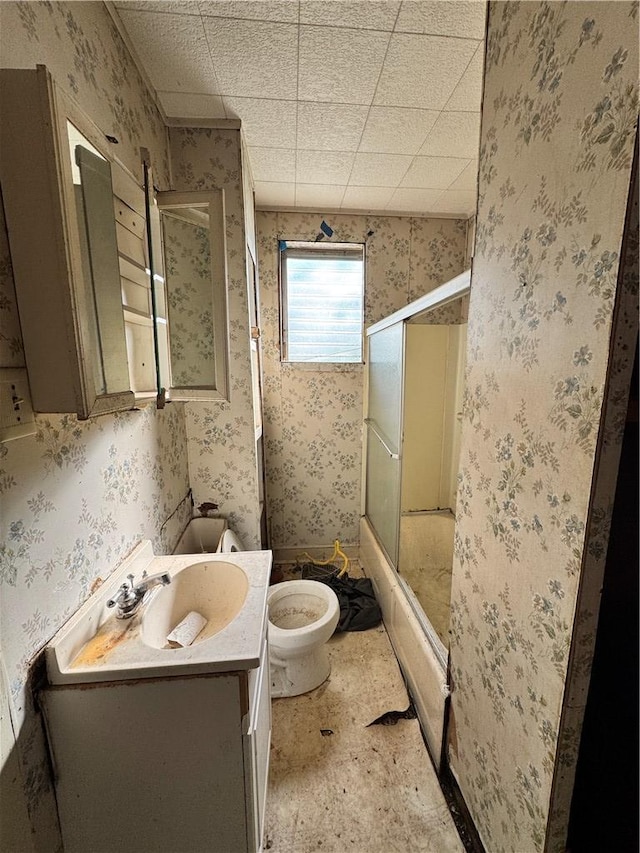 bathroom with toilet, wallpapered walls, vanity, and bath / shower combo with glass door