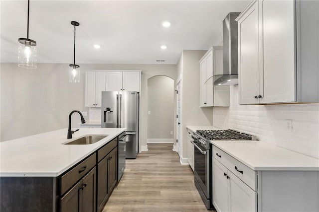 kitchen with tasteful backsplash, wall chimney range hood, stainless steel appliances, arched walkways, and a sink