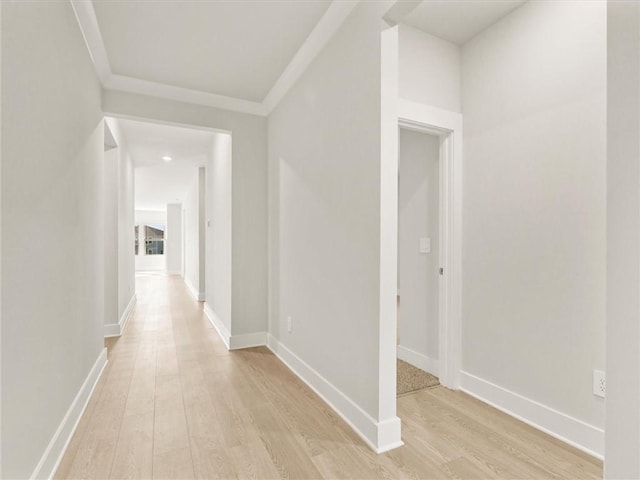 corridor with light wood-style flooring, crown molding, and baseboards