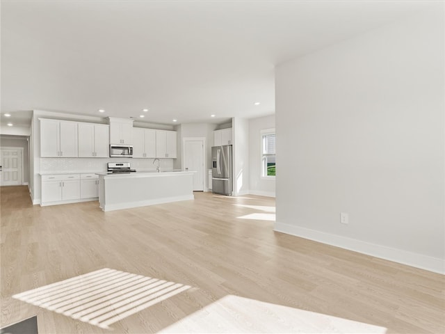 unfurnished living room featuring a sink, light wood finished floors, recessed lighting, and baseboards