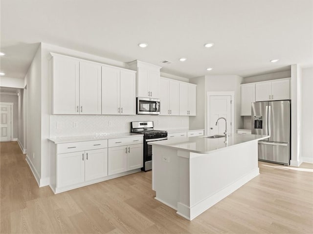 kitchen with appliances with stainless steel finishes, a sink, tasteful backsplash, an island with sink, and light wood-style flooring